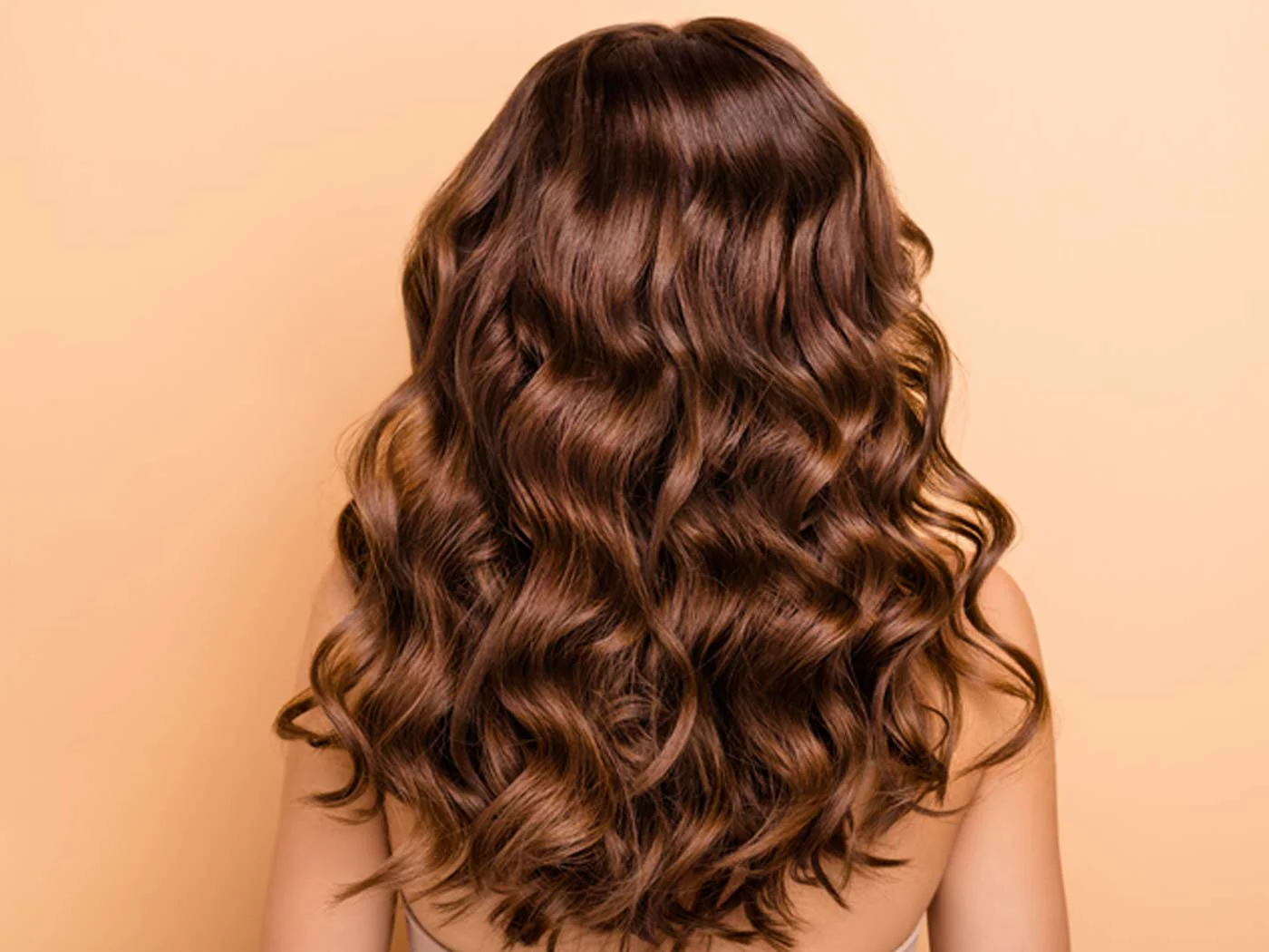 Brunette deep wave wig on a human head with an orange wall background.