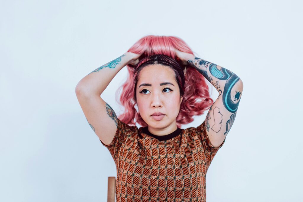 A woman with pink hair and tattoos poses indoors, showcasing a bold fashion style.