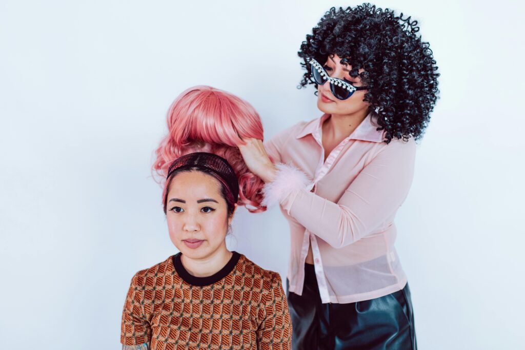 A stylist adjusts a bright pink wig on a model, showcasing fun hair fashion.